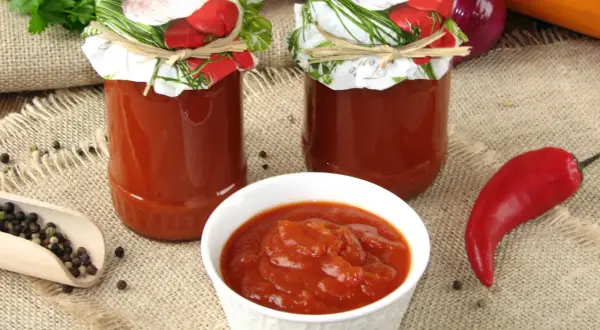 Domowy ketchup z cukinii w słoikach, miseczce i z papryczką chili.