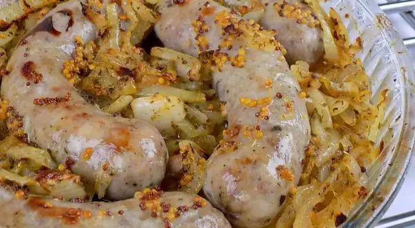 Pyszna biała kiełbasa pieczona w cebuli i musztardzie, z chrupiącymi ziarnami gorczycy. Aromatyczne danie w szklanej formie.