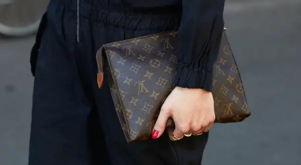 Dłoń trzyma brązową kopertówkę Louis Vuitton z monogramem.
