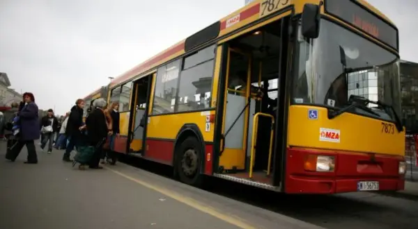 Żółto-czerwony autobus miejski z otwartymi drzwiami, pasażerowie wsiadają.