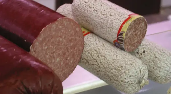 Kawałki ciemnej i jasnej kiełbasy salami, jedna przekrojona.