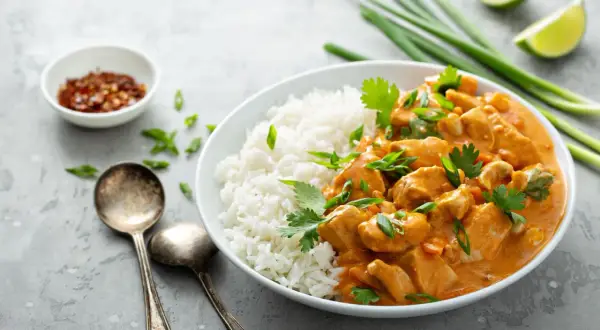 Kurczak w sosie curry z ryżem, posypany szczypiorkiem i kolendrą. Obok miseczka z chili i limonka.