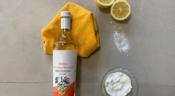 Bottiglia di aceto di vino bianco, limoni, panno giallo e bicarbonato: ingredienti naturali per uno sgrassatore fatto in casa.