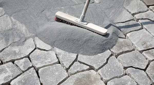 Besen verteilt feinen Fugensand auf Pflastersteinen. Der Sand dient als effektiver Fugensand gegen Unkraut und stabilisiert die Steine.