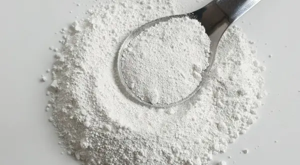 Biały proszek na łyżce i rozsypany na powierzchni. Czy to potencjalna **titanium dioxide szkodliwość**?