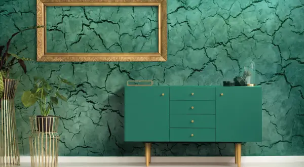 Parete con finitura in stucco materico verde intenso, incorniciata da un elegante mobile verde e piante in vasi dorati.