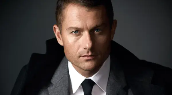 James Badge Dale w szarym garniturze i czarnym krawacie, z niebieskimi oczami wpatrującymi się w obiektyw.