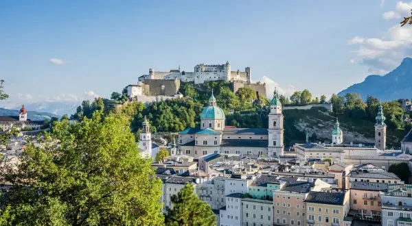 Widok na zamek Hohensalzburg i katedrę w Salzburgu, serce ziemi salzburskiej, z zielonymi drzewami w tle.