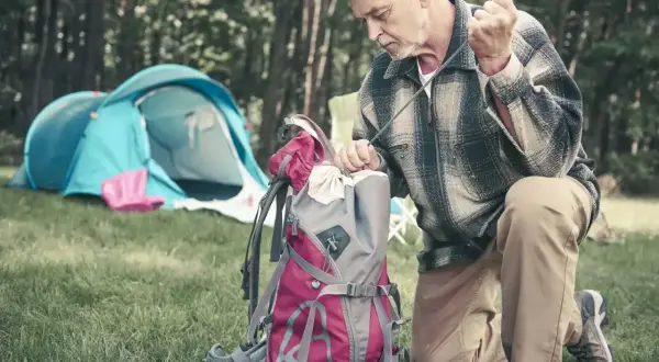 Mężczyzna pakuje plecak, przygotowując się do wyprawy. W tle rozstawiony namiot. Idealny zestaw, by wiedzieć, co zabrać w góry na 5 dni.