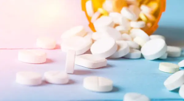 Białe tabletki rozsypane z pomarańczowego pojemnika. Czy to opium? Nie, to leki.