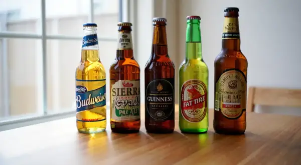 Cinque bottiglie di birra, tra cui Budweiser, Sierra Nevada e Guinness, pronte per essere raffreddate. La temperatura birra in frigo è ideale per gustarle al meglio.