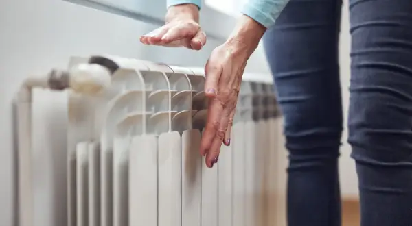 Dłonie sprawdzają temperaturę grzejnika, zastanawiając się, dlaczego grzejnik jest zimny na dole.