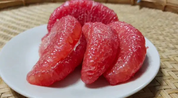 Soczyste kawałki różowego grejpfruta na białym talerzyku. Codzienne spożywanie grejpfruta może przynieść wiele korzyści zdrowotnych.
