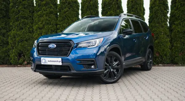 Błękitny Subaru Ascent z czarnymi felgami stoi przed żywopłotem.