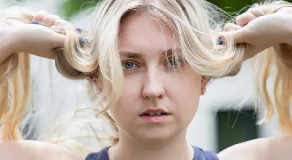 Blondes Haar, das mit Kamillentee behandelt wurde, zeigt vorher-nachher-Effekte. Die Frau hält ihre blonden Zöpfe hoch.