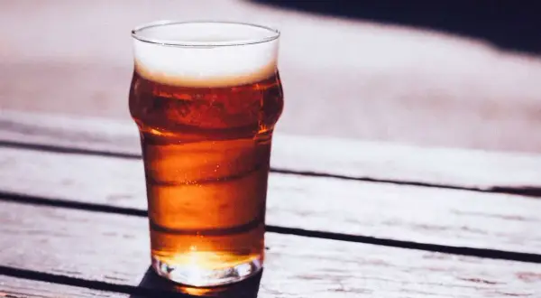 Un bicchiere di caña birra con schiuma bianca, illuminato dal sole, su un tavolo di legno all'aperto.