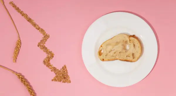 Strzałka z ziaren pszenicy wskazuje na kromkę chleba na talerzu, symbolizując uczulenie na gluten i potrzebę unikania go.