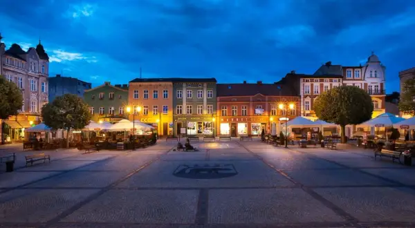 Wieczorny rynek w Kościerzynie, z oświetlonymi kamienicami i ogródkami restauracyjnymi.