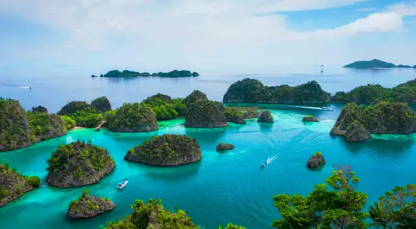 Rajskie krajobrazy Raja Ampat: turkusowa woda, bujna zieleń i łodzie sunące po spokojnym morzu.
