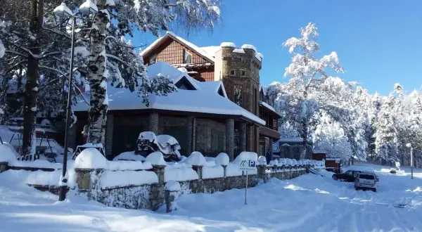Un hermoso paisaje de Albania en invierno, con una casa cubierta de nieve y árboles nevados bajo un cielo azul brillante.