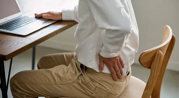 Homme assis à un bureau, se tenant le bas du dos. Il se demande combien de temps d'arrêt pour une discopathie.