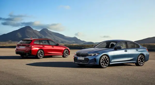 Dwa nowe BMW Serii 3 2025: niebieski sedan i czerwone kombi, stoją na pustkowiu z górami w tle.