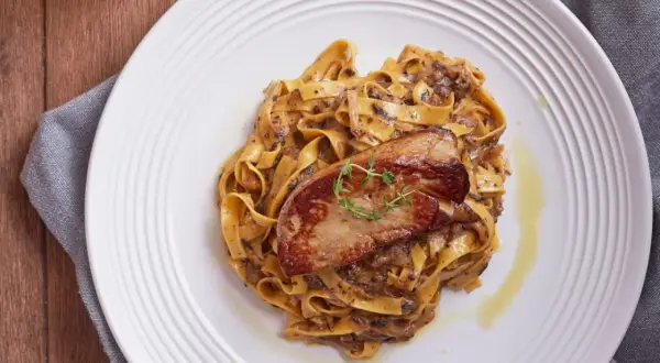 Pasta con foie gras, un plato gourmet con un trozo dorado de foie gras sobre una cama de fettuccine cremoso.