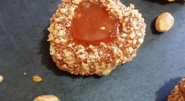 Un sablé algérien à la confiture, enrobé de noisettes concassées, sur fond sombre.
