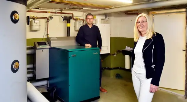 Ein Mann und eine Frau stehen neben einem grünen Nano BHKW-Gerät in einem Heizungsraum.