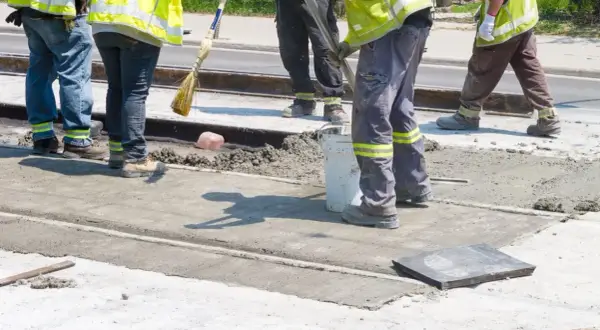 Prace interwencyjne: robotnicy w kamizelkach odblaskowych wylewają beton na torowisko.