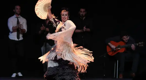 Bailaora con abanico y mantón, evocando el espíritu de Lorca y el flamenco, acompañada por guitarrista y palmeros.