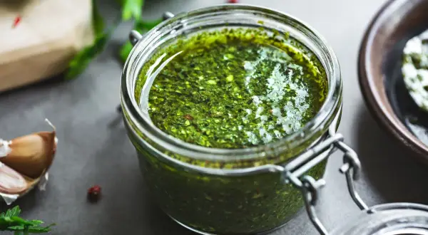 Słoik domowego pesto z bazylii, obok czosnek i świeże zioła. Idealne do makaronu.