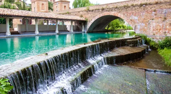 Cascata d'acqua cristallina sotto un antico ponte in mattoni, un angolo di pace tra i borghi medievali umbri.