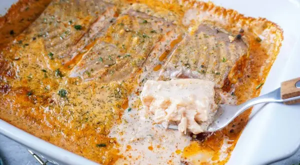 Saftiges Lachsfilet in cremiger Sahnesauce, ein köstliches Lachs Sahne Gratin, wird mit einer Gabel herausgehoben.