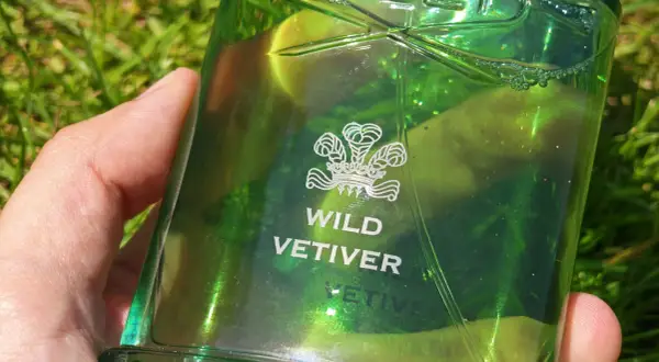 Zielona butelka perfum Creed Wild Vetiver w dłoni na tle trawy.