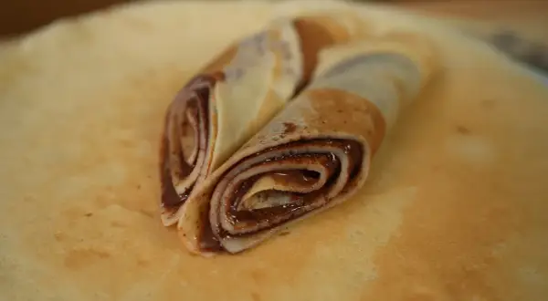 Zwei gerollte low carb pfannkuchen mit Schokoladencreme, auf einem größeren Pfannkuchen liegend.