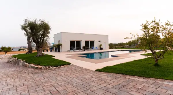 Pavimentazione esterna texture con blocchi di pietra color ruggine e beige, che circonda una piscina moderna e un prato verde.