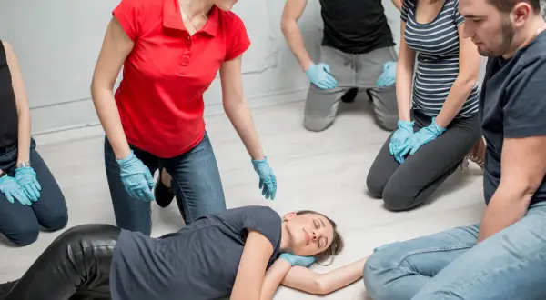 Erste-Hilfe-Kurs: Eine Frau in Rot zeigt die stabile Seitenlage. Ein Merksatz hilft beim Erinnern.
