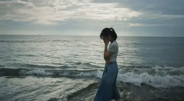 Kobieta na plaży, zakrywająca twarz dłońmi, symbolizuje objawy depresji.
