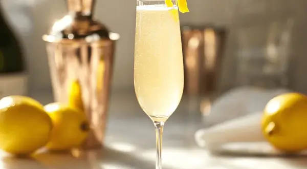 En elegant French 75 med citronskal, bredvid citroner och en kopparskakare.
