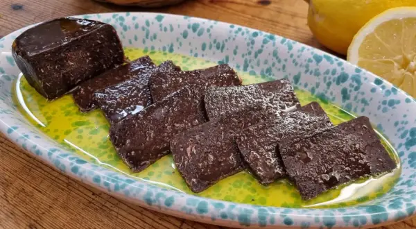 Fette di salame di tonno scuro, lucido e saporito, servite in una ciotola con olio verde e limone.