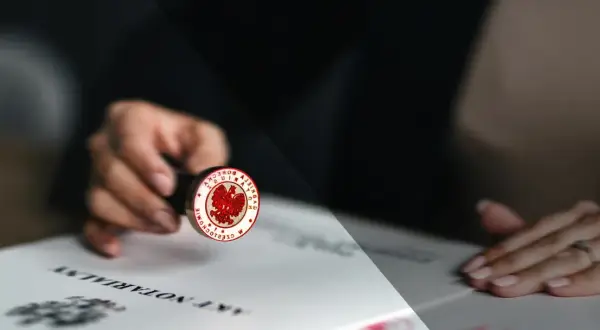 Dłoń trzyma pieczęć notarialną z orłem, gotową do złożenia podpisu na akcie poświadczenia dziedziczenia.