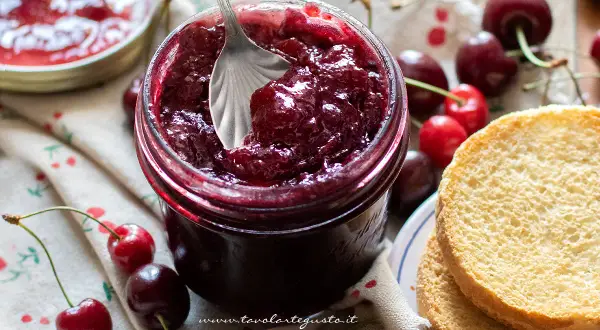 Un barattolo pieno di deliziosa marmellata di ciliegie, pronto per essere spalmato su fette biscottate.