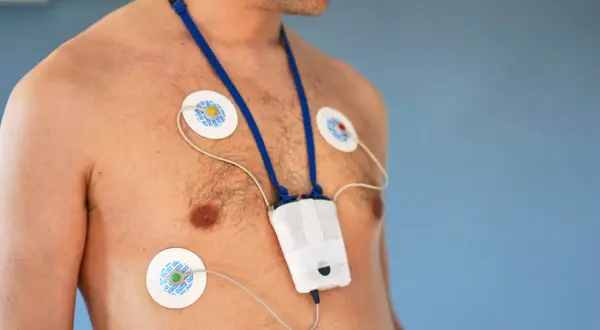 Mężczyzna z przyklejonymi elektrodami do klatki piersiowej i zawieszonym na szyi urządzeniem. To holter, który monitoruje pracę serca.