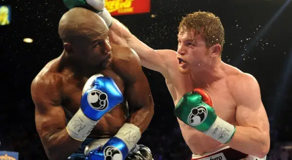 Two boxers exchange blows, one with a blue boxing guard, the other with a green one. Sweat flies as they fight.