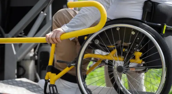 Persona in sedia a rotelle si aggrappa a un corrimano giallo, suggerendo un noleggio auto con legge 104 per maggiore accessibilità.