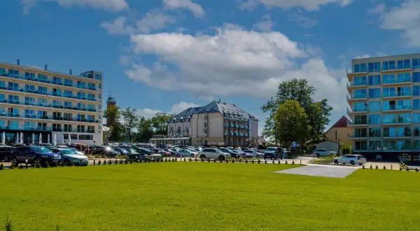 Nowoczesne budynki hotelowe i parking pełen samochodów na tle błękitnego nieba z chmurami.