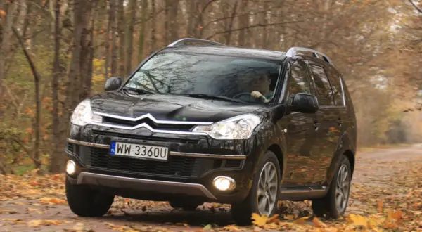 Czarny Citroen C-Crosser jedzie po leśnej drodze pokrytej jesiennymi liśćmi.