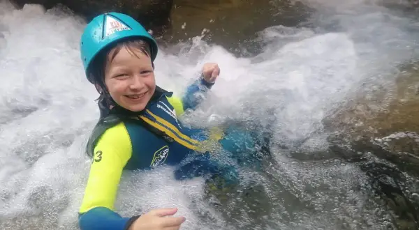 Niño sonriente con casco y traje de neopreno disfrutando del barranquismo en la Sierra de Guara. ¡Una aventura de senderismo acuático inolvidable!