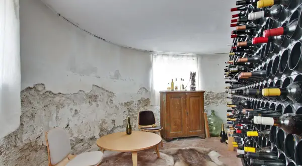 En vinkällare med en imponerande samling flaskor, perfekt för att lagra vin hemma. Ett runt bord med stolar och en gammal skåp ger rummet karaktär.